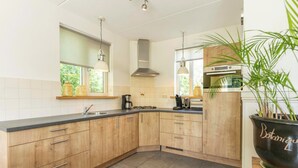 Een moderne keuken met houten kastjes, een zwart aanrecht en een grote zwarte plantenbak met groene planten.