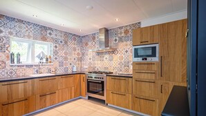 A kitchen with patterned tiles, wooden cabinets, a stove, and a microwave. - Holiday Home in De Koog Near Beach (De Koog)