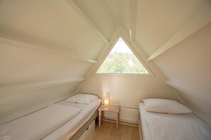 A small, triangular attic bedroom with two single beds and a nightstand. - Holiday Home Groote Keeten Near Beach (Callantsoog)