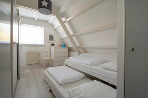 A bedroom with bunk beds, a radiator, a chair, and a window with blinds. - Sandepark 165 Holiday Home Near Beach (Callantsoog)