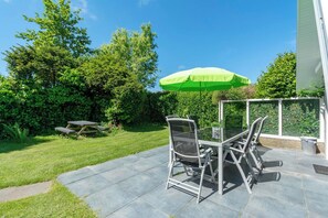 An outdoor patio with a table and chairs, a green umbrella, and a stone-tiled floor. - Sandepark 165 Holiday Home Near Beach (Callantsoog)