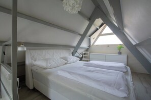 A bedroom with a bed, bedside table, lamp, and a window with a plant. - Sandepark 165 Holiday Home Near Beach (Callantsoog)