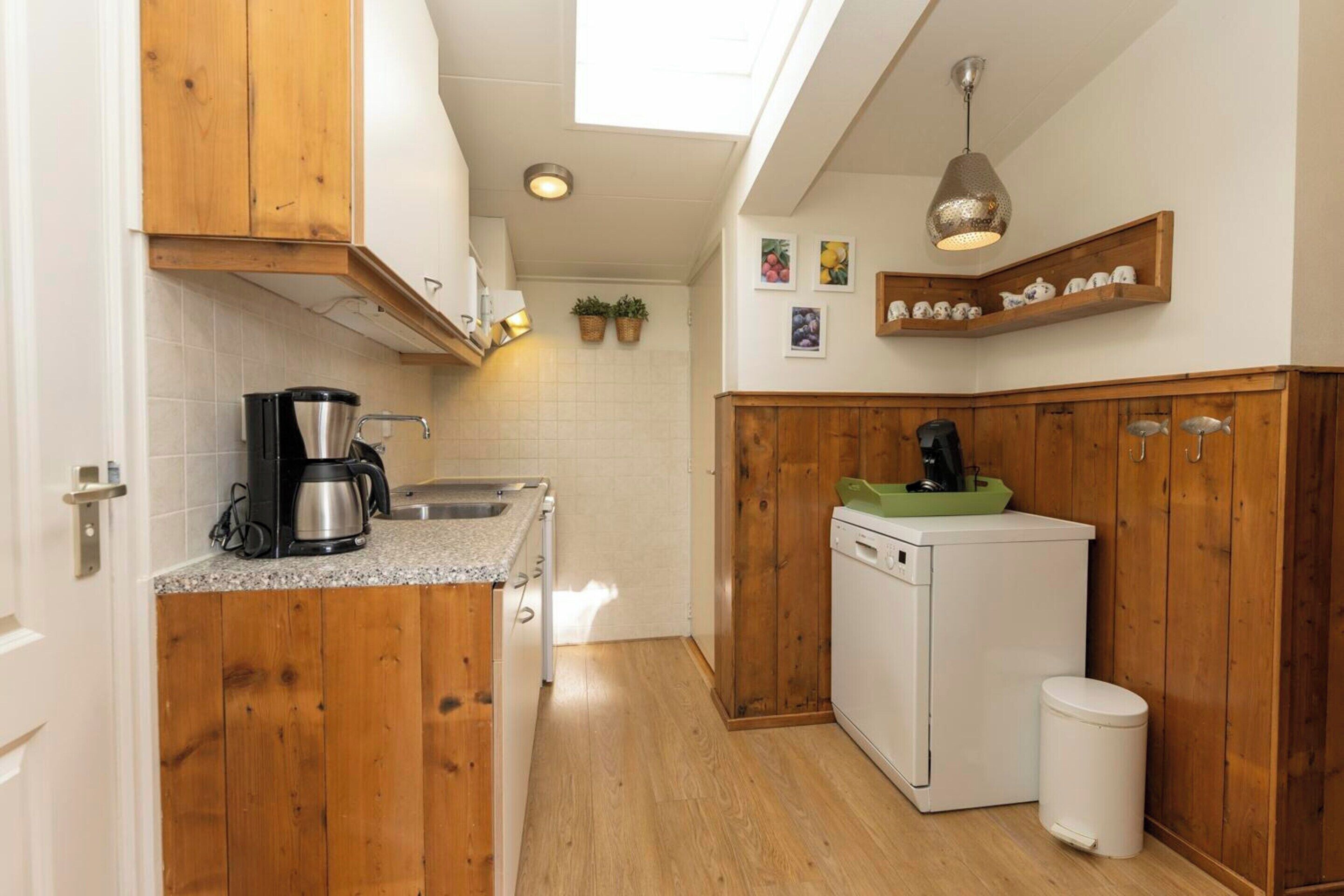 A compact kitchen with wooden cabinets, a coffee maker, a dishwasher, and a small trash bin.