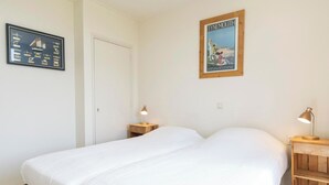 Una camera da letto con due letti, un comodino in legno con una lampada, un poster incorniciato al muro e una porta.