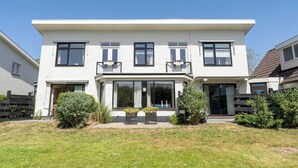 Una casa a due piani con tetto piatto, ampie finestre e un portico con piante in vaso.