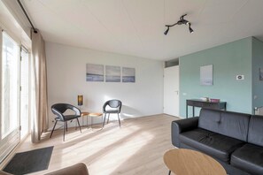 A modern living room with a black leather sofa, a wooden coffee table, and two black chairs. There is a small side table with a lamp, and a painting on the wall. - Beachside Escape w/ Terrace (Julianadorp)