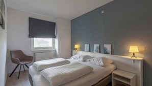 Ein Schlafzimmer mit einem Bett, Nachttischlampen, einem Sessel und einem Fenster mit Blick.