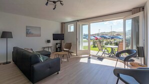 Ein modernes Wohnzimmer mit Sofa, Sesseln, Fernseher und einem Balkon mit Blick auf Autos und Hügel.