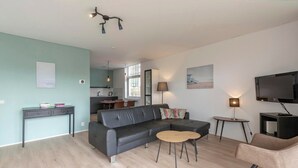 Ein modernes Wohnzimmer mit einem schwarzen Ledersofa, einem Couchtisch, einem Fernseher und einem Essbereich mit Tisch und Stühlen.