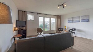 Ein modernes Wohnzimmer mit einer Couch, Sesseln, einem Fernseher und Kunstwerken an der Wand.
