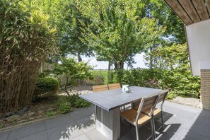 An outdoor patio with a table and chairs, surrounded by lush greenery and trees. - Elegant Holiday Home With Terrace (Burgerbrug)
