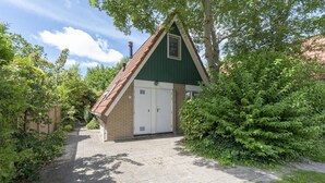 Un petit bâtiment d’un seul étage, doté d’un toit végétalisé et d’une porte blanche, entouré de verdure et bordé d’un chemin pavé.