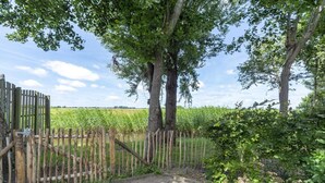 Une porte en bois mène à un chemin pavé bordé d’arbres et donnant sur un champ.