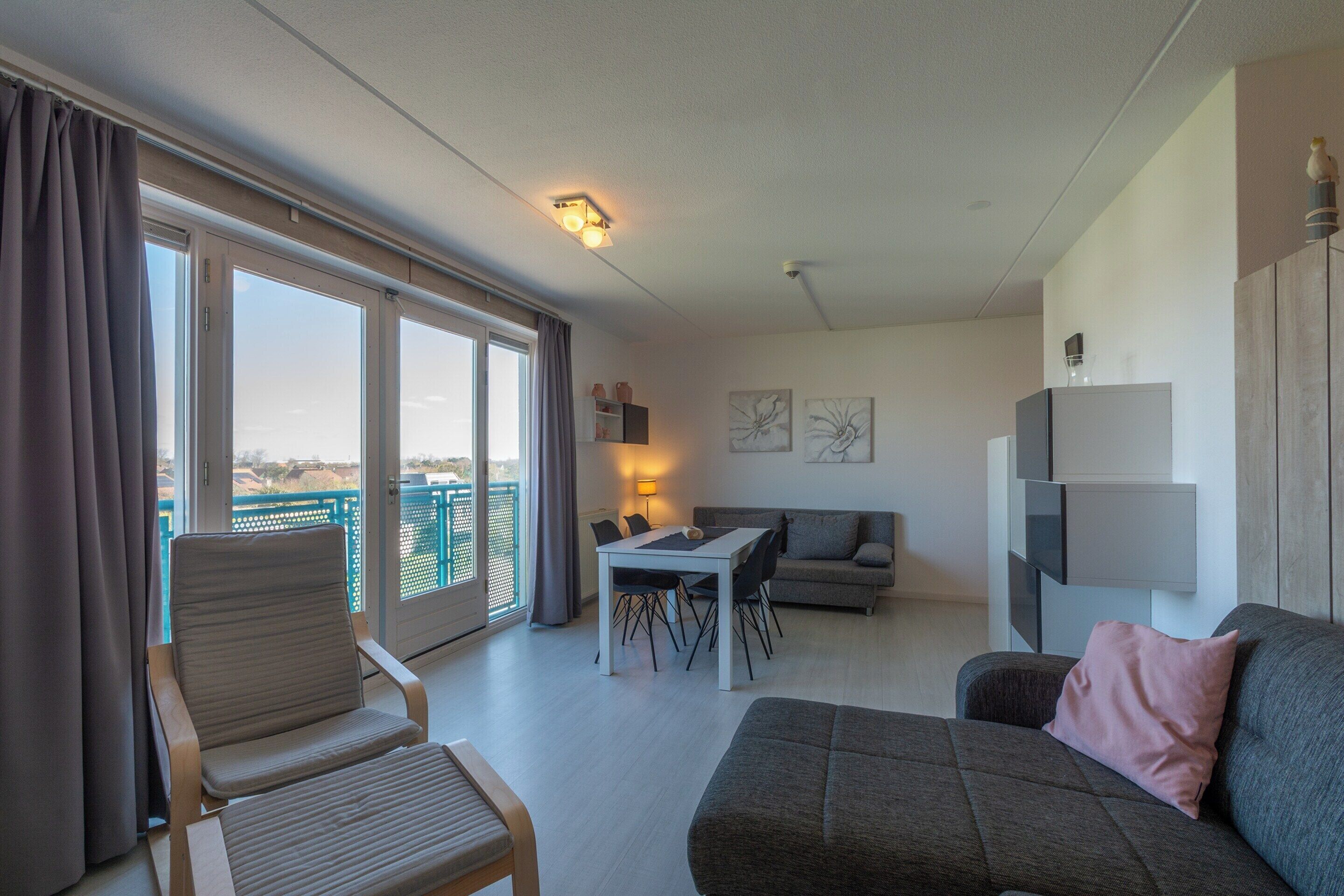 A modern living room with a sofa, armchair, dining table, and a balcony with a view.