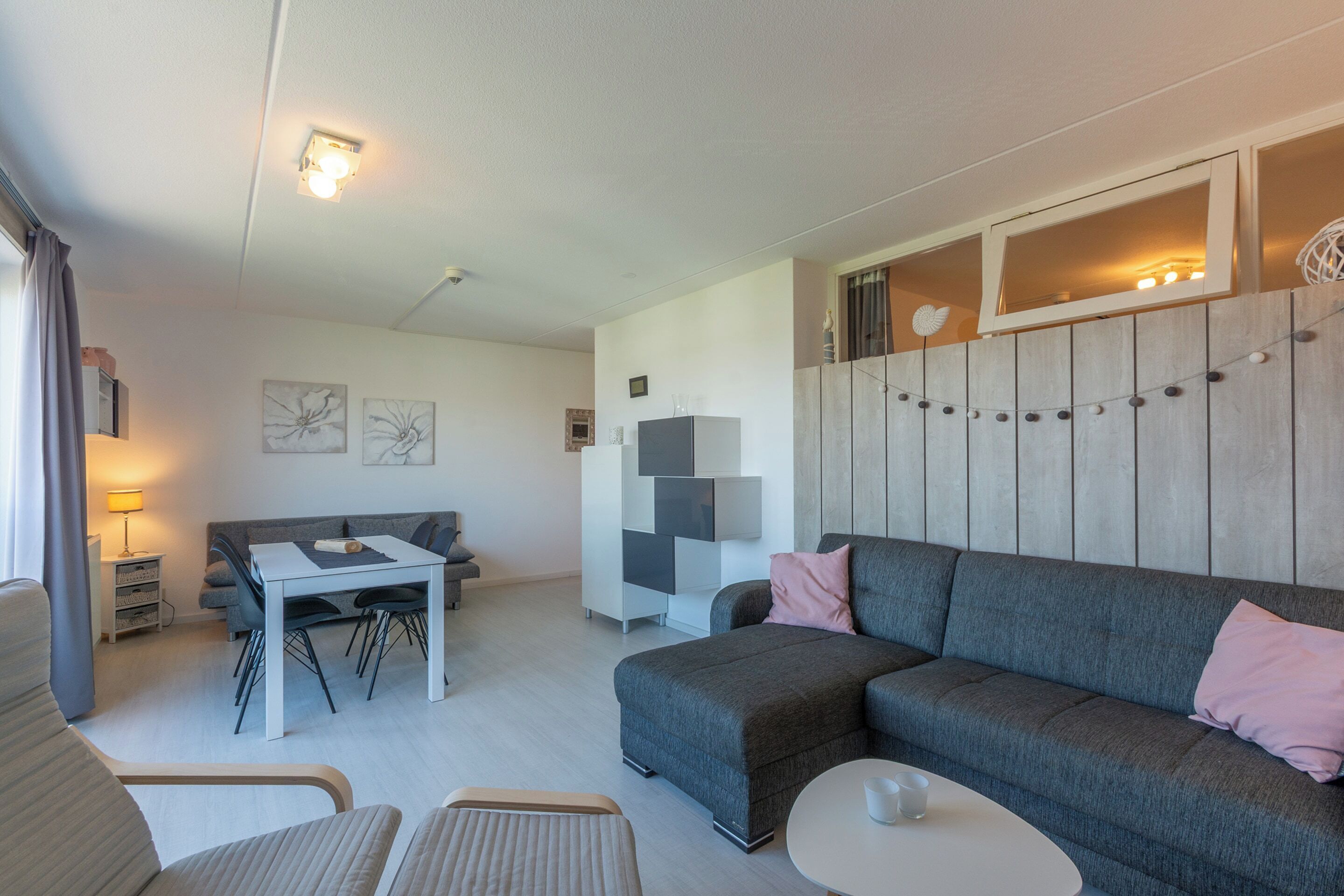 A modern living room with a grey sofa, a dining table, and a small white table.