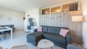 En moderne stue med en grå hjørnesofa, et hvidt sofabord og et spiseområde med et hvidt bord og stole.