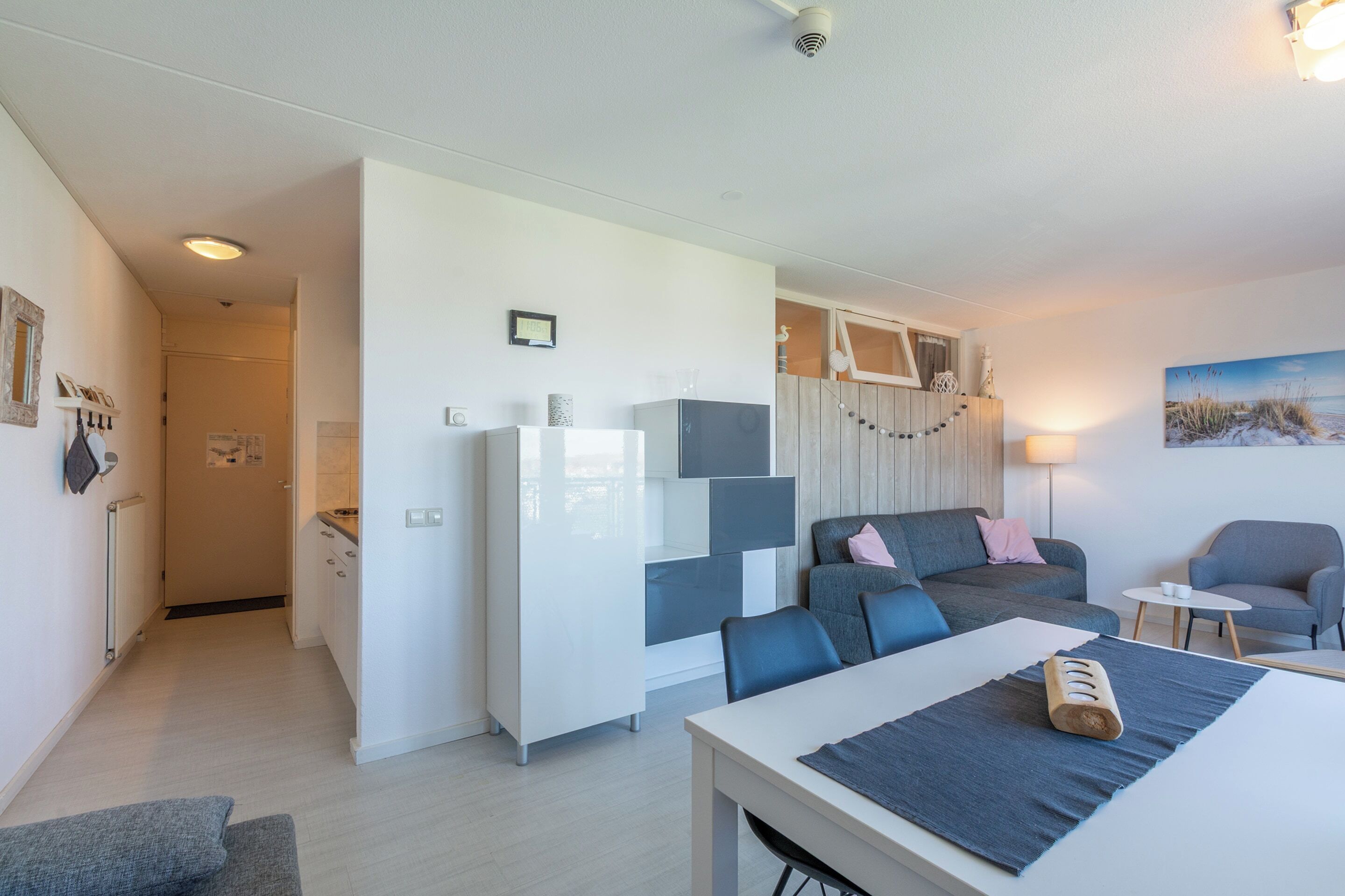 Een moderne woonkamer met een bank, stoelen, een eettafel en een keukenhoek.