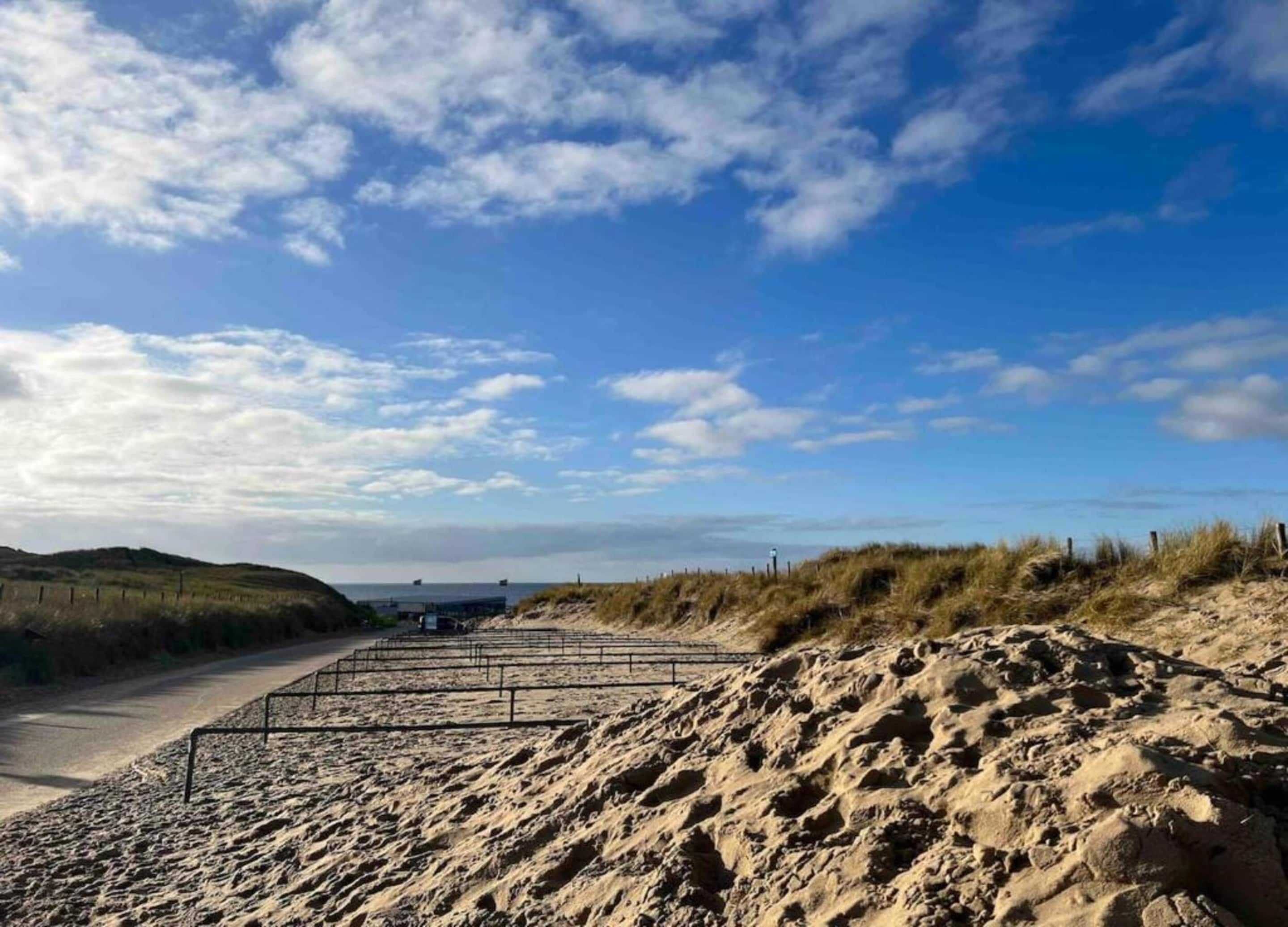 A sandy beach with a clear sky and dunes in the background.