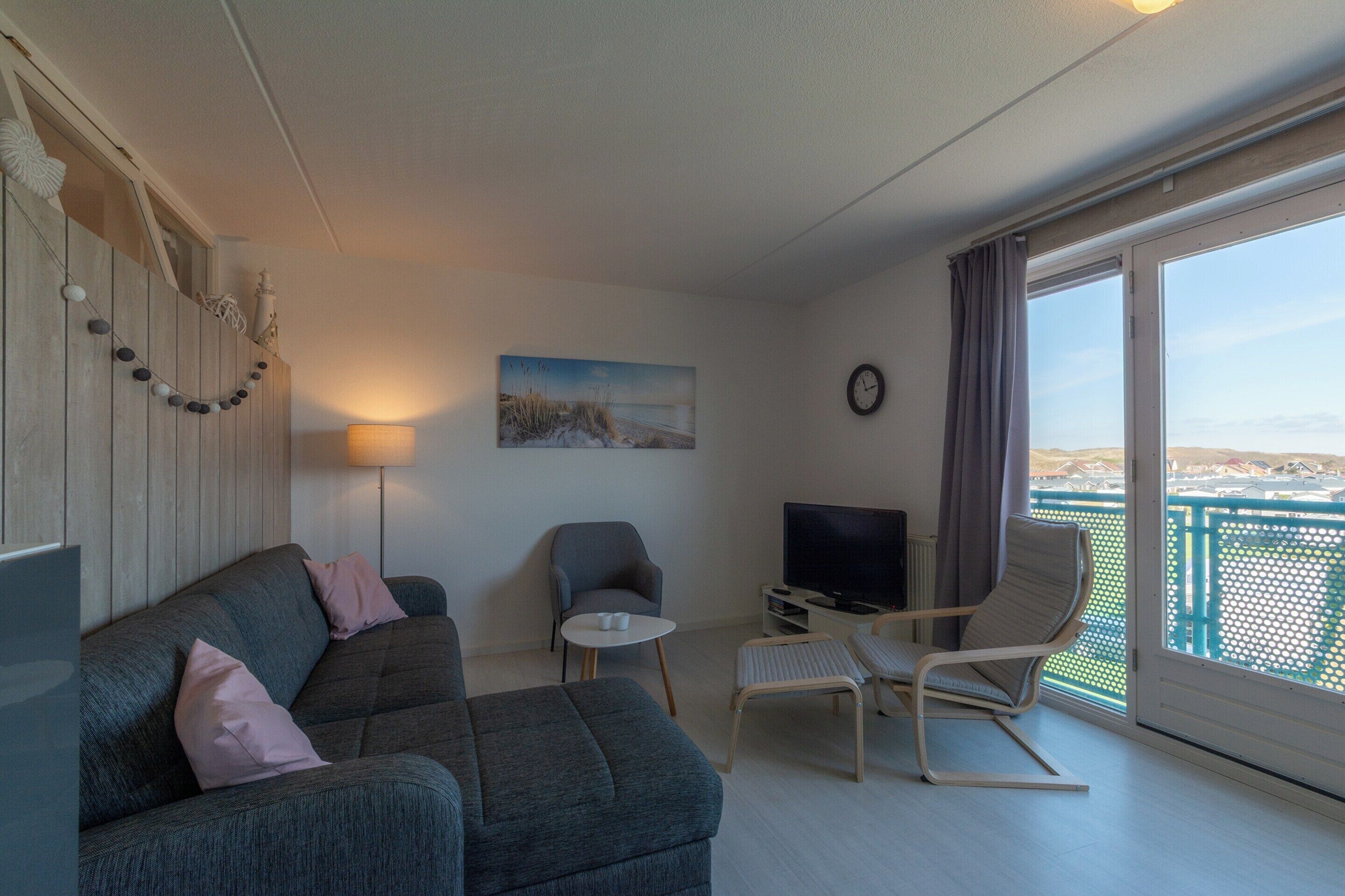 Un salon moderne avec un canapé, des fauteuils, un téléviseur et un balcon offrant une vue agréable.