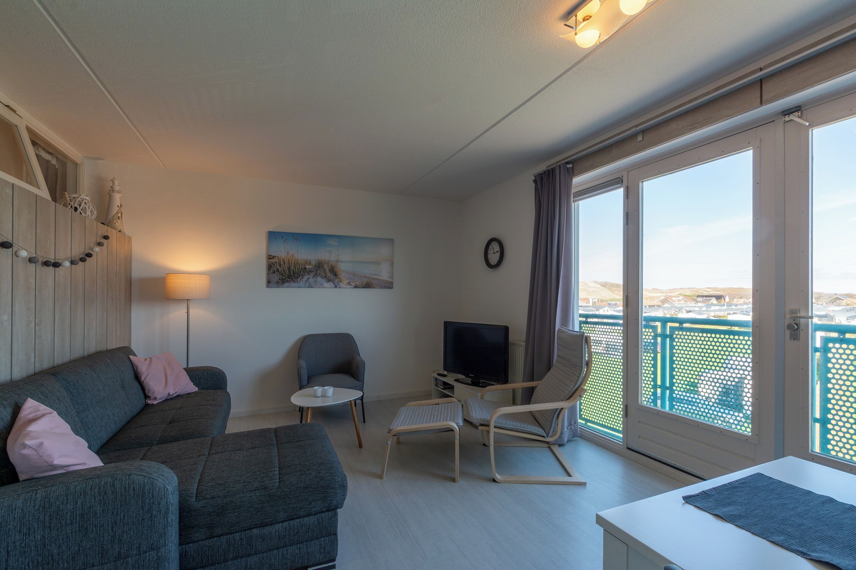 A modern living room with a sofa, armchairs, a TV, and a balcony with a view.