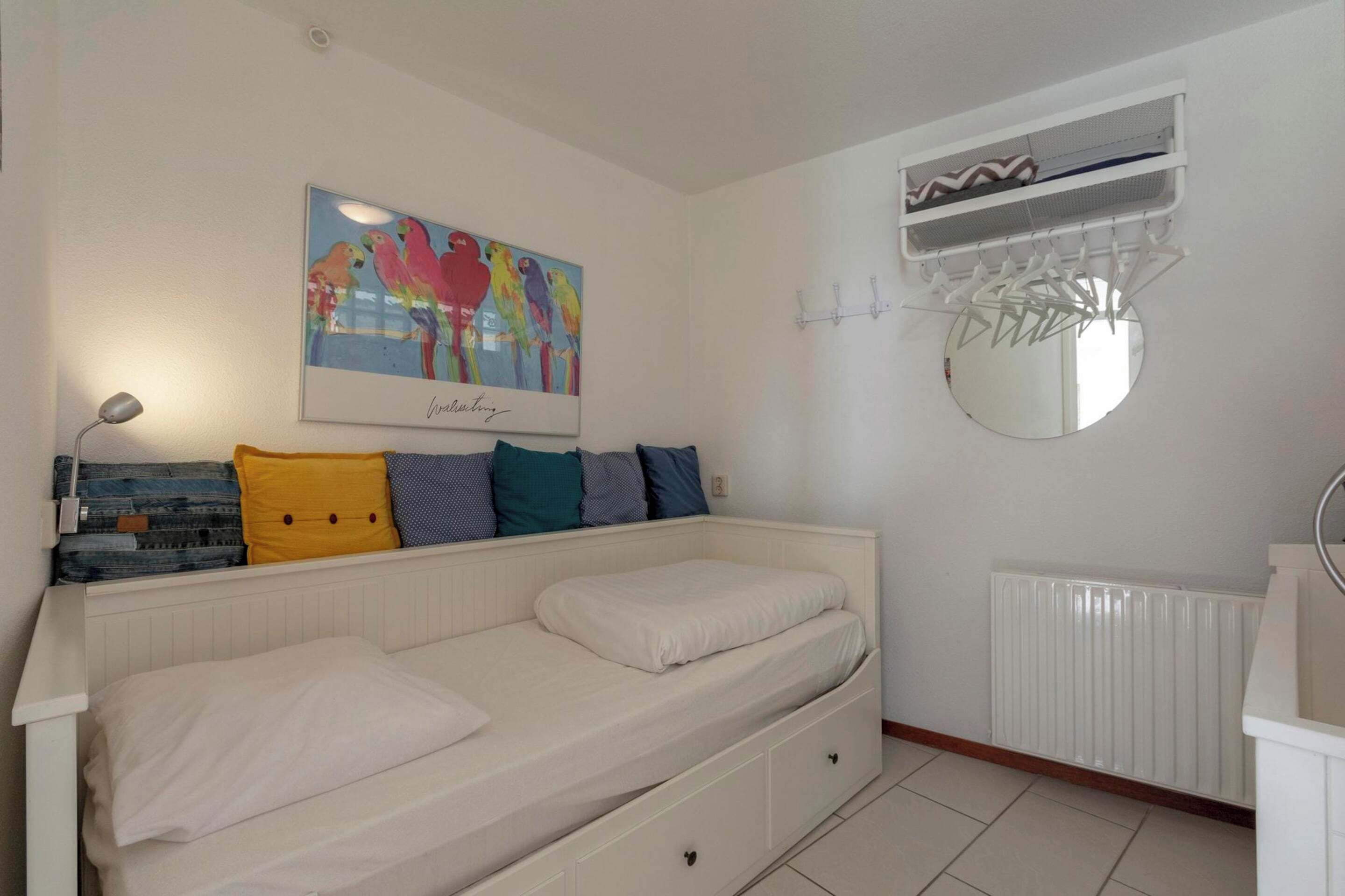 A bedroom with a bed, a wall-mounted air conditioning unit, a radiator, and a framed artwork above the bed.
