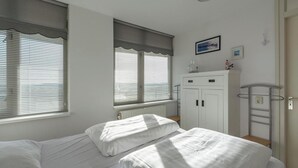 A bedroom with two beds, a radiator, a wardrobe, and a window with blinds.