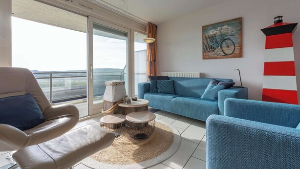 A modern living room with a sofa, armchair, and round coffee table. There is a large window with a view of the outdoors.