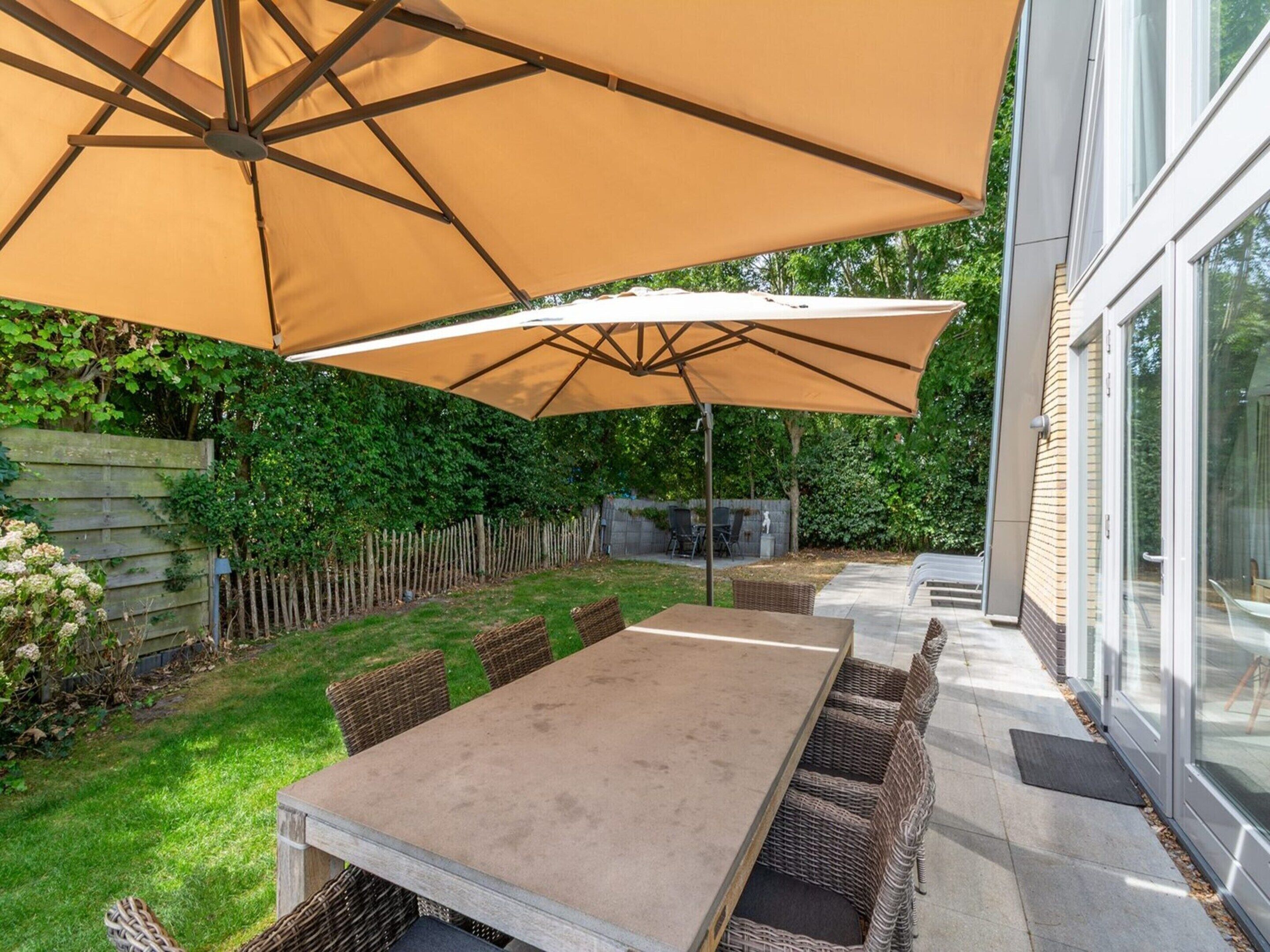 Un patio con una mesa, sillas, un paraguas y un edificio de vidrio al fondo.