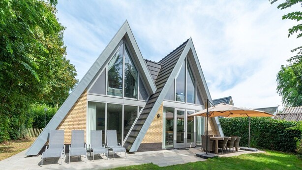 Ein modernes Haus mit einem dreieckigen Dach, großen Fenstern und einer Terrasse mit Gartenmöbeln.