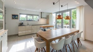 Eine moderne Küche mit Essbereich, großen Fenstern und Pendelleuchten.