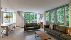 Ein modernes Wohnzimmer mit Essbereich, großen Fenstern und Blick auf Grünflächen.