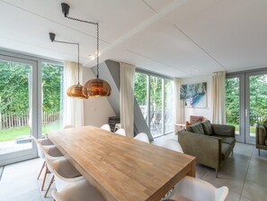 Ein geräumiger Essbereich mit Holztisch und weißen Stühlen, große Fenster mit Blick auf einen Garten und ein modernes Interieur.
