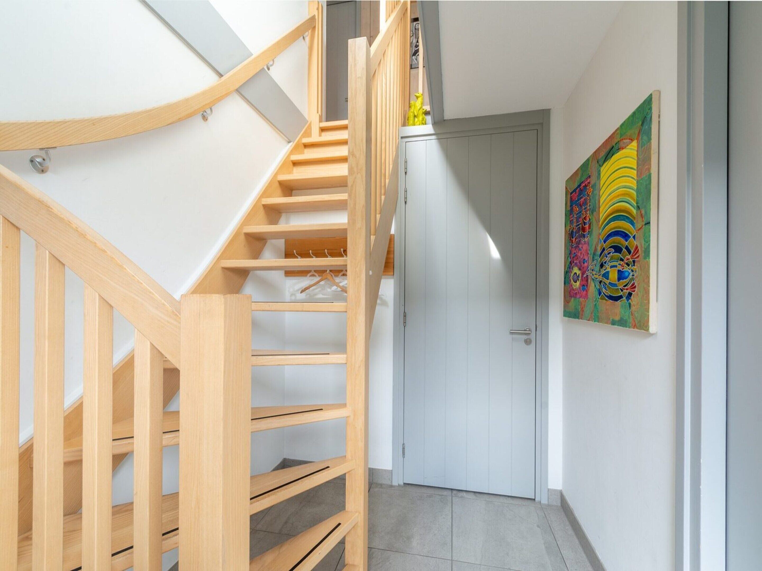 A wooden staircase leading to a room with a white door and a colorful abstract painting on the wall.
