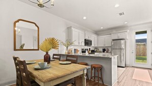 A modern kitchen with white cabinets, stainless steel appliances, a wooden dining table, and a large island.