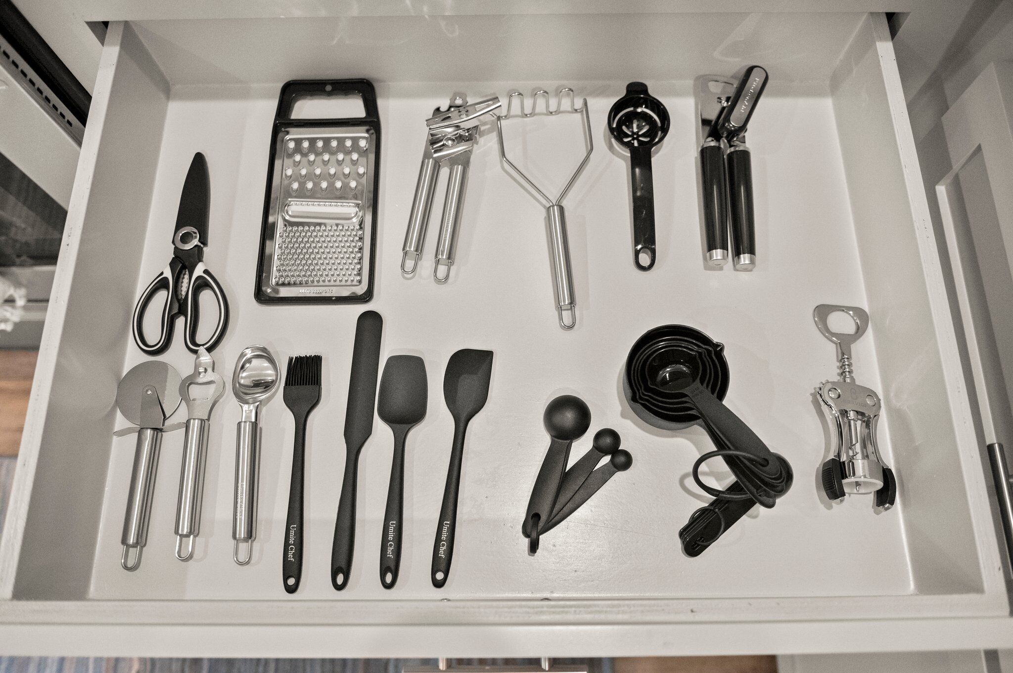 Un tiroir contenant divers ustensiles de cuisine, notamment des ciseaux, une râpe, des spatules et un ouvre-boîte.