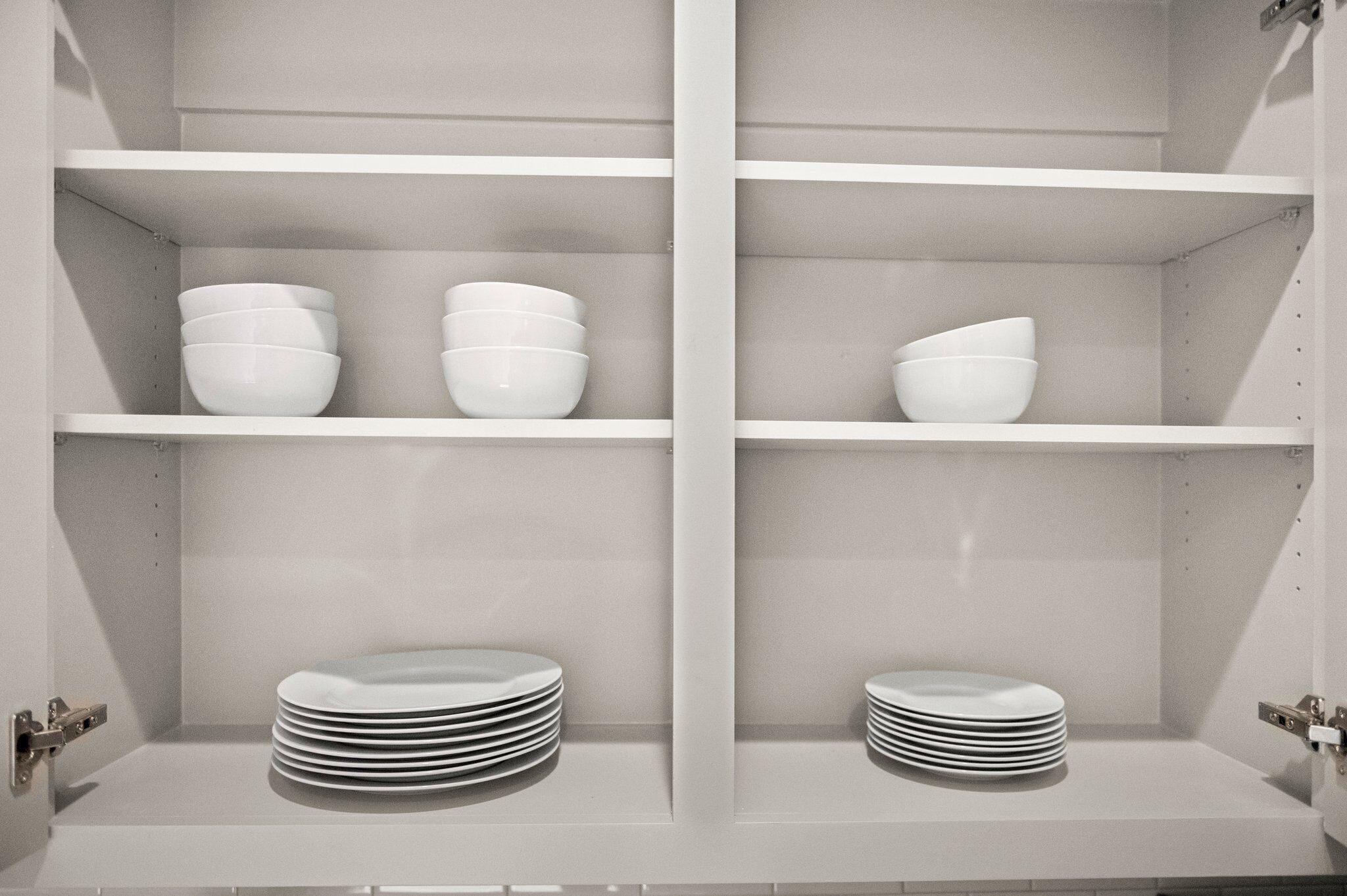 Una cocina con armarios y estanterías blancas, que contiene cuencos y platos blancos.