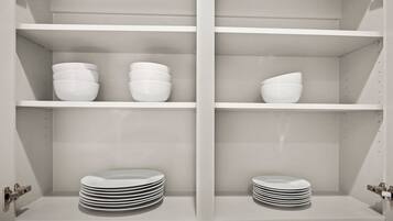 Una cocina con armarios y estanterías blancas, que contiene cuencos y platos blancos.
