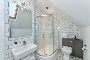 Ein modernes Badezimmer mit einer Duschkabine, einem weißen Waschbecken, einer Toilette und einem Schminktisch mit Spiegel.