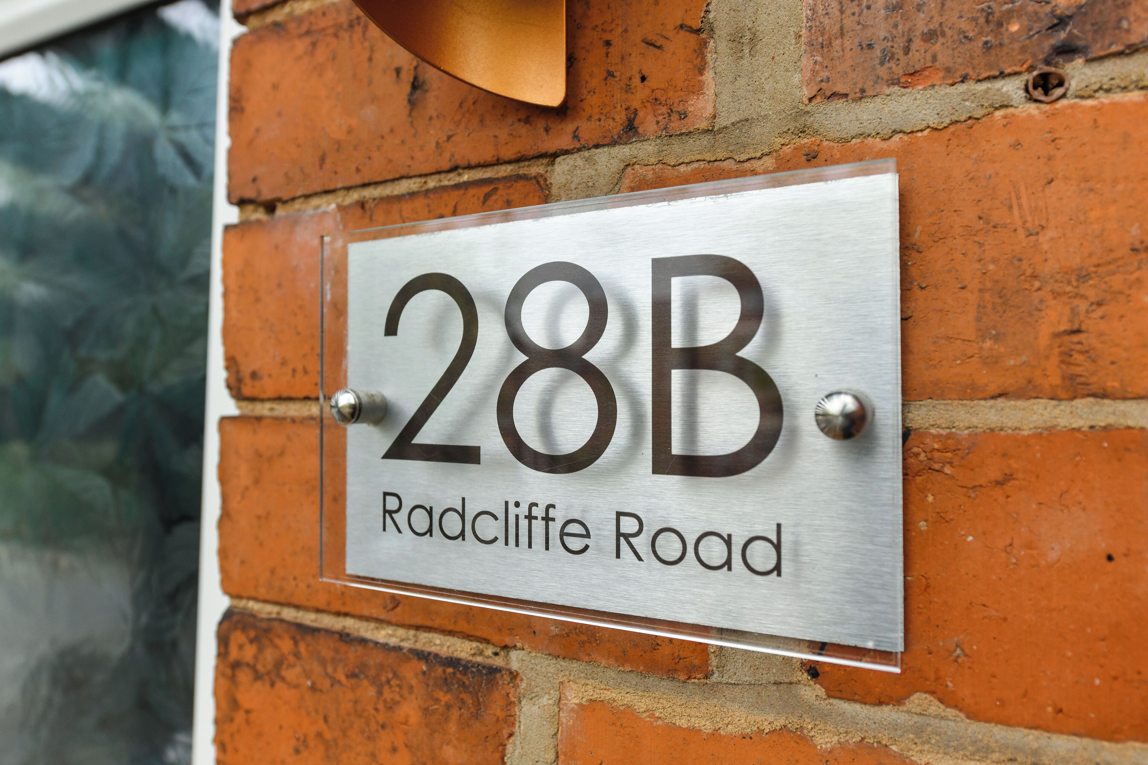 A metal house number sign with '28B' and 'Radcliffe Road' on a brick wall.
