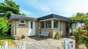 A two-story house with a visible front door, a bench outside, and a white picket fence. - Bungalow in Sint Maartenszee Near Beach (Sint Maartensvlotbrug)