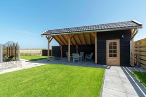 Une structure en bois, dotée d’un toit recouvert de tuiles, d’une porte et d’un espace détente avec des chaises.