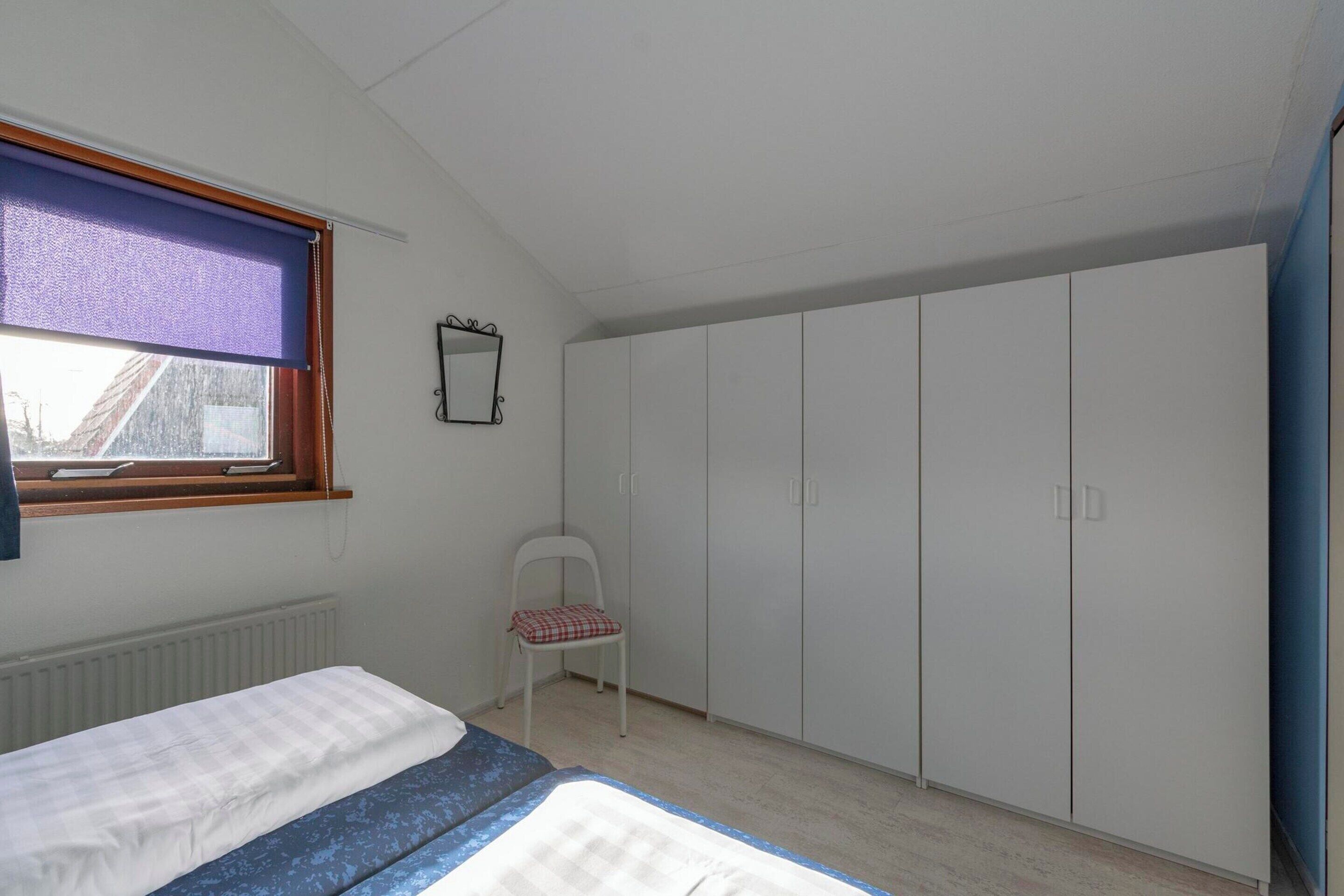 Quarto com cama, cadeira, guarda-roupa e janela com cortina.