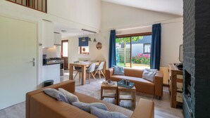 A modern living room with a sofa, coffee table, and a fireplace. There is a kitchen area with a dining table and chairs. - Yperhof 66 Holiday Home for 6 Guests on Cost (Julianadorp)