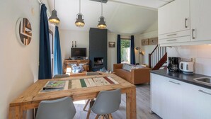 A cozy living room with a fireplace, a dining area with a wooden table, and a kitchen with white cabinets and a coffee maker. - Yperhof 66 Holiday Home for 6 Guests on Cost (Julianadorp)