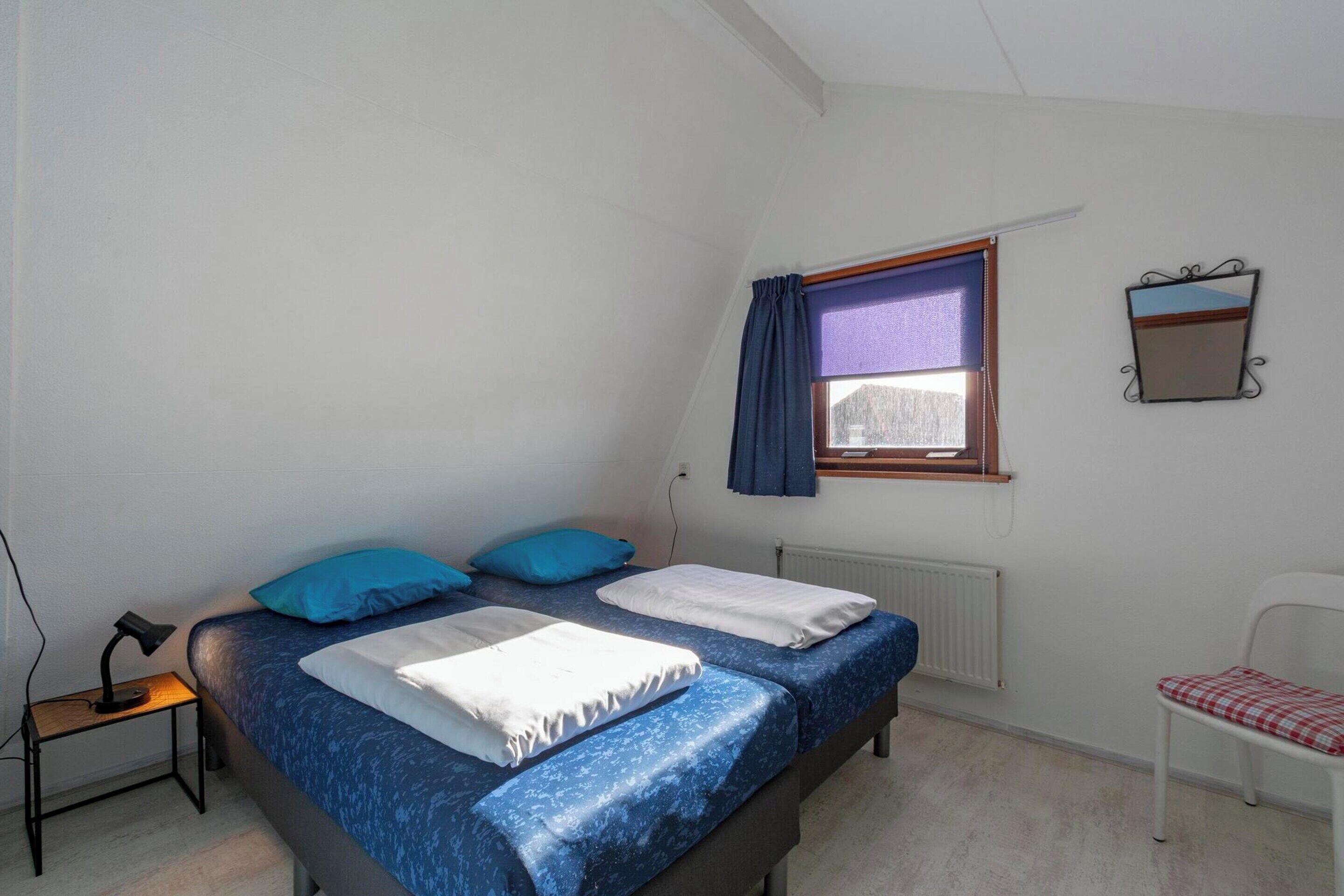 A bedroom with a bed, a chair, a desk, and a window with curtains.