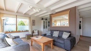 A modern living room with a grey sofa, a wooden coffee table, and a large mirror on the wall. - Wildrijk 152 Holiday Home in Sint Maartenszee (Sint Maartensvlotbrug)