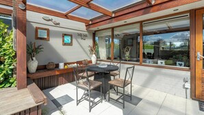 A patio with a round table and chairs, a wooden bench, and a glass enclosure with a view of the garden. - Wildrijk 152 Holiday Home in Sint Maartenszee (Sint Maartensvlotbrug)