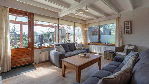 A spacious living room with a large sofa set, a wooden coffee table, and a view of the outdoors through large windows. - Wildrijk 152 Holiday Home in Sint Maartenszee (Sint Maartensvlotbrug)