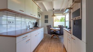 A modern kitchen with white cabinets, a wooden countertop, and a dining area with a table and chairs. - Wildrijk 152 Holiday Home in Sint Maartenszee (Sint Maartensvlotbrug)
