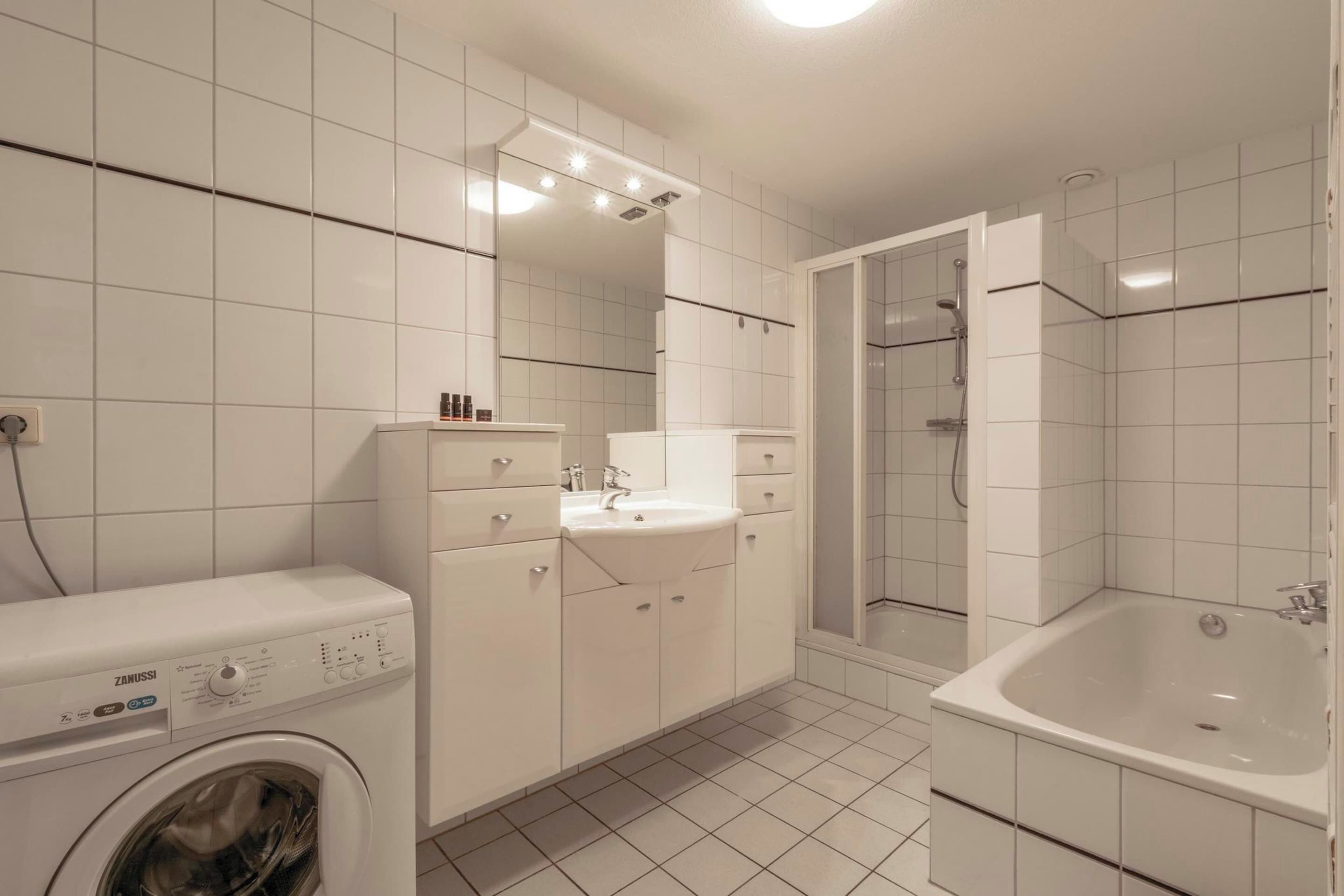 Une salle de bain moderne équipée d’un lave-linge, d’un lavabo, d’un miroir et d’une baignoire.
